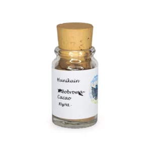 Kleines Glasfläschchen mit beigem Korken, gefüllt mit Rapé (beigem Pulver). Weißes Etikett mit schwarzer Schrift: Hunikuin Theobroma Cacao.