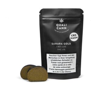 Verpackung von Sahara Gold CBD-Hasch von Qualicann, mit einem CBD-Gehalt von unter 32% und THC unter 1%. Vor der Verpackung liegen zwei Stücke des goldbraunen Haschs.